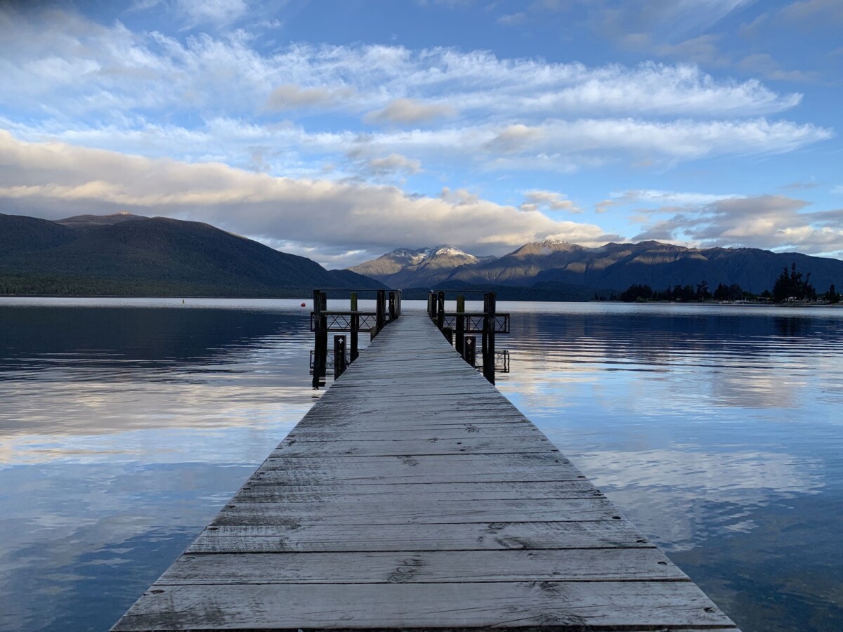 tranquil boardwalk leading to a serene lake in southland with mountainous backdr | Two Scots Abroad Tranquil boardwalk leading to a serene lake in Southland, with mountainous backdrop.