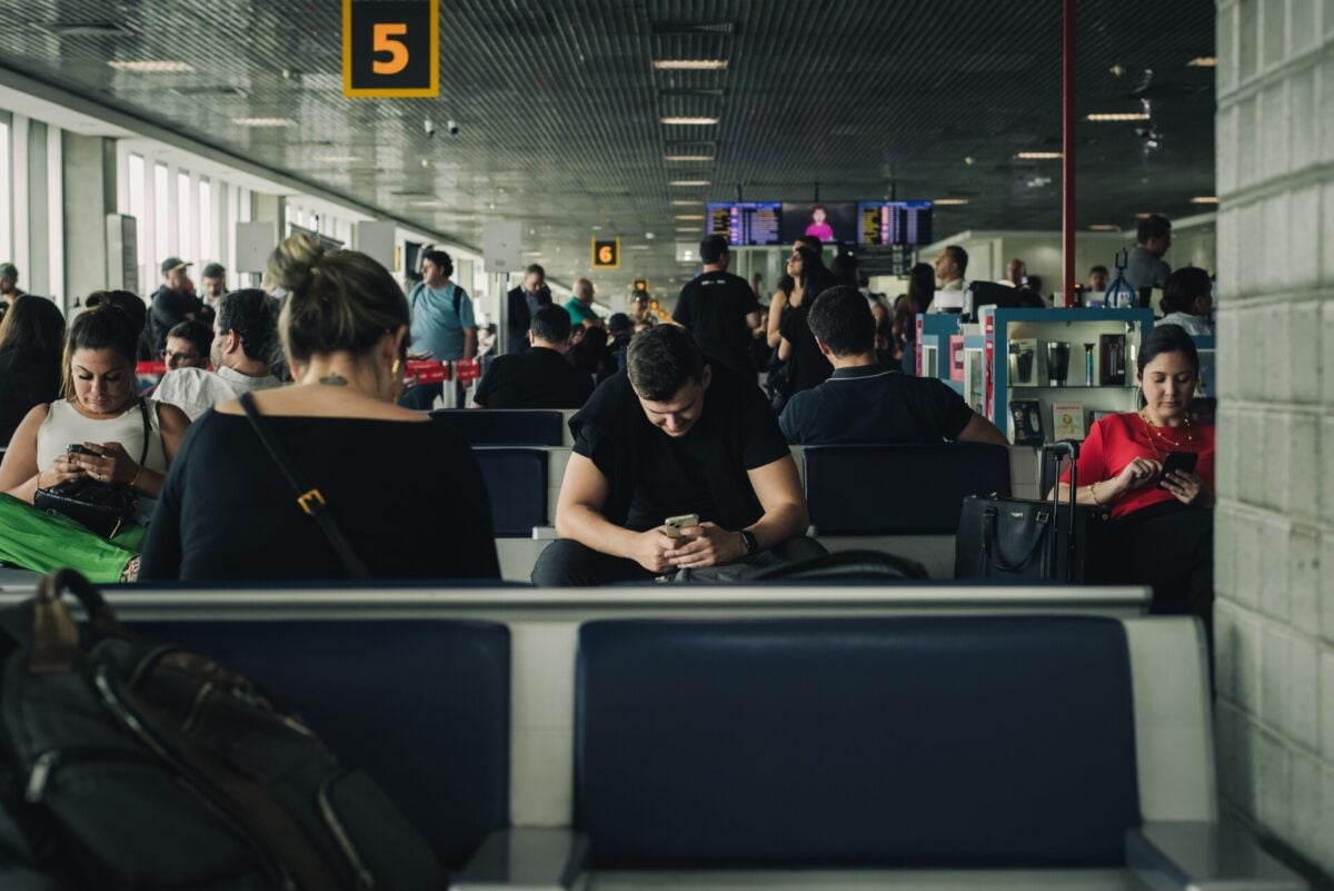 travelers seated and waiting at sao paulo airport terminal engaging with smartph | Two Scots Abroad Travelers seated and waiting at São Paulo airport terminal, engaging with smartphones.