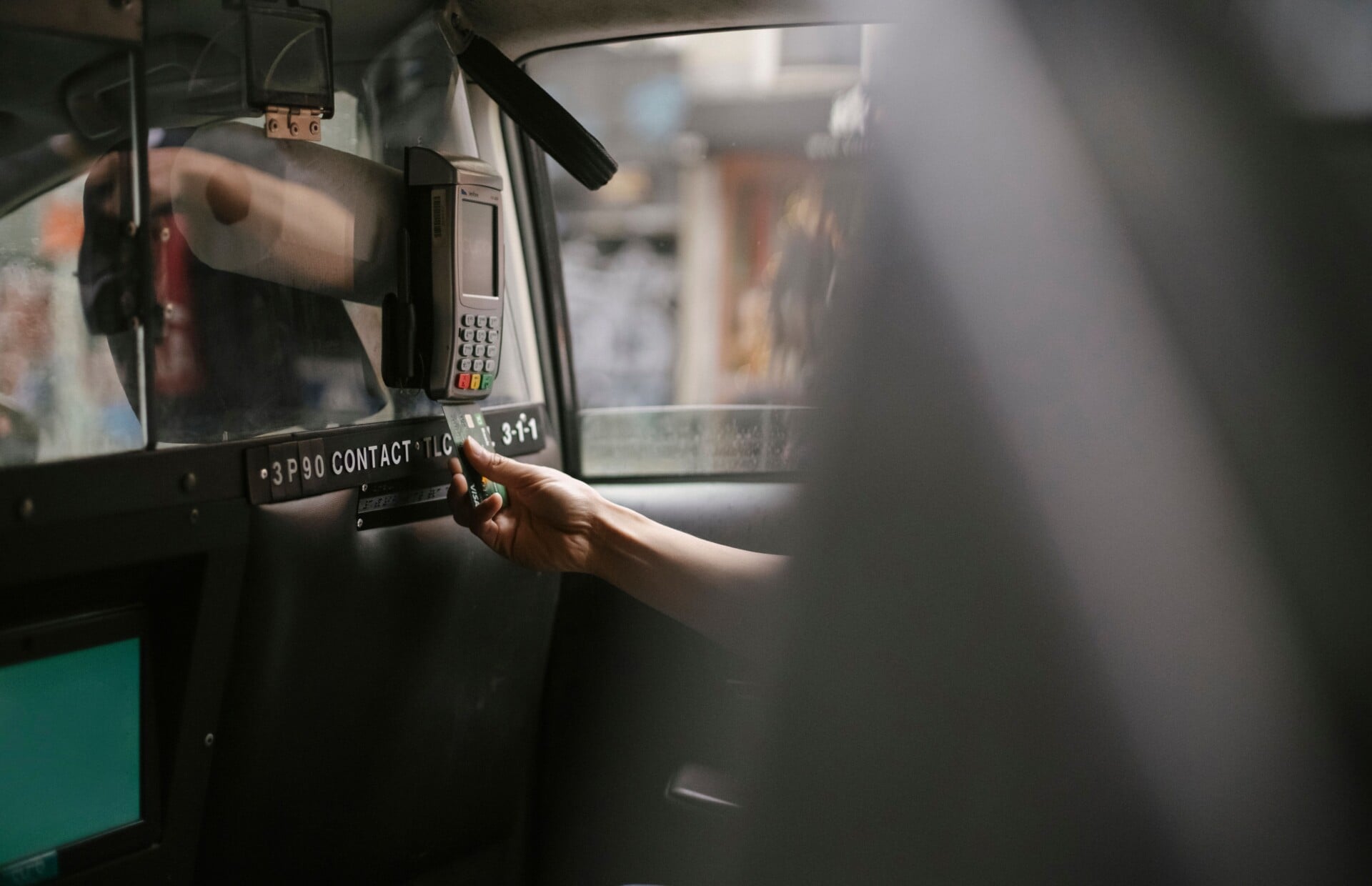 Unrecognizable person sitting in taxi car and paying by credit card and payment terminal in daytime