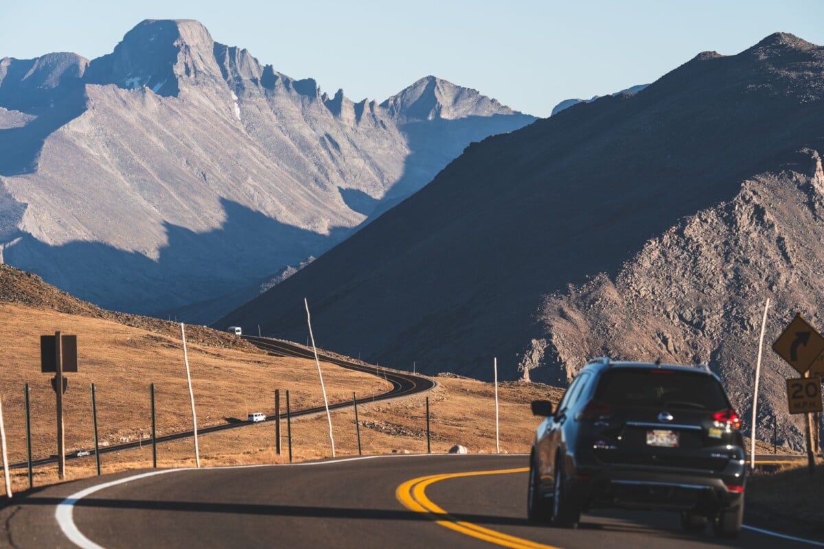 A car on a winding mountain road beneath Colorado peaks