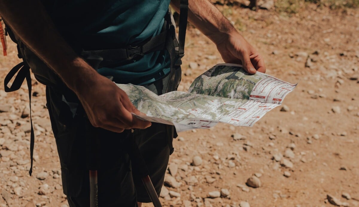 a hiker studies a map on a sunny day exploring a rugged outdoor trail | Two Scots Abroad A walker checking a paper map on an unpaved trail