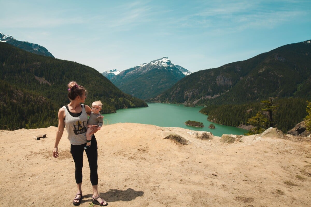 a mother holding her child enjoys a scenic mountain view by a turquoise lake on | Two Scots Abroad A mother holding her child enjoys a scenic mountain view by a turquoise lake on a sunny day.
