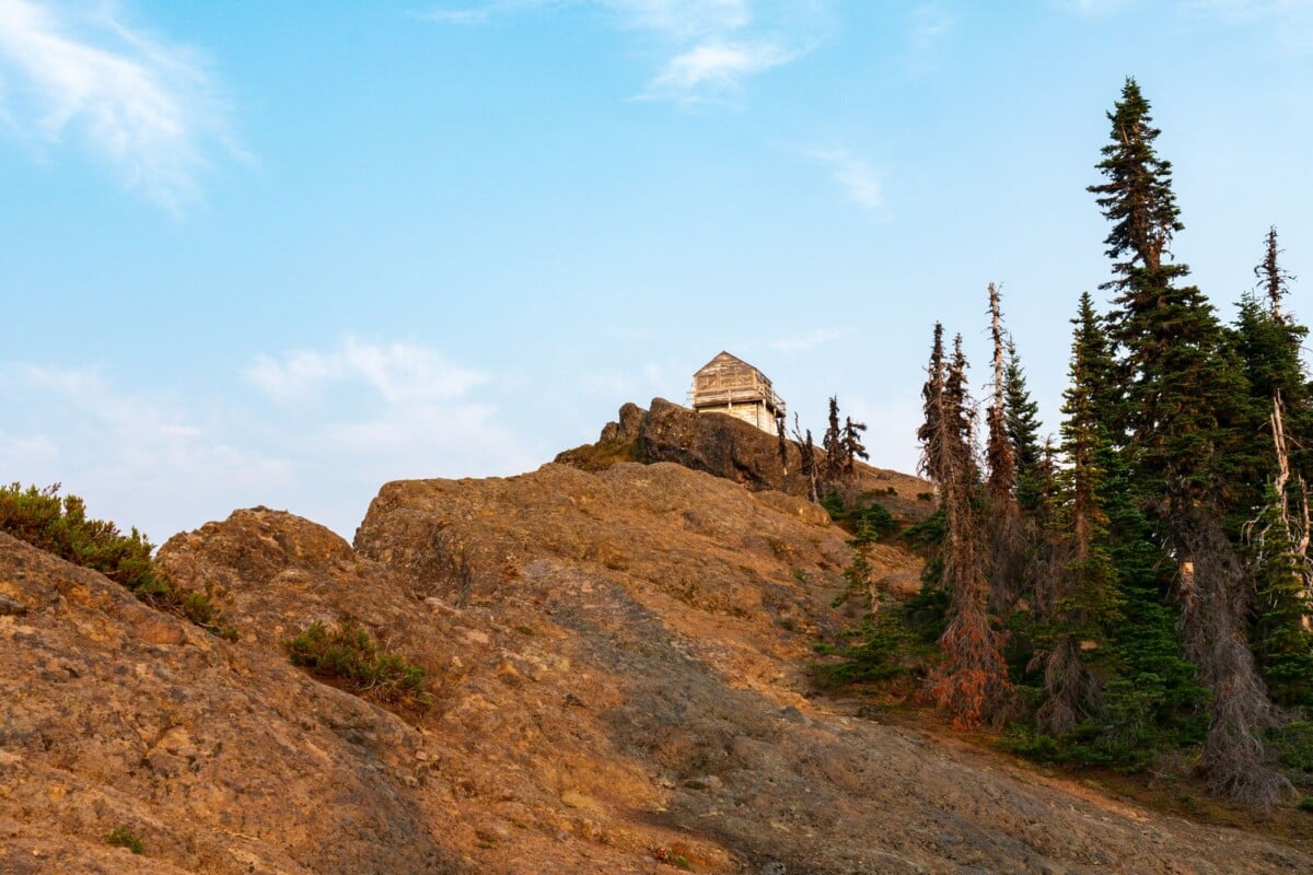 a rustic lookout cabin perched atop a rocky mountain ridge in ashford wa under a | Two Scots Abroad A rustic lookout cabin perched atop a rocky mountain ridge in Ashford, WA under a blue sky.