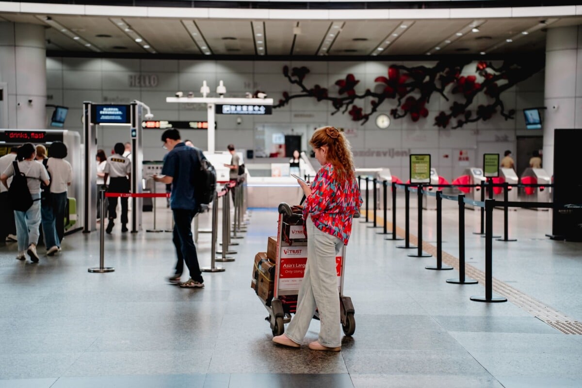 a traveler checks her phone while waiting with a luggage cart at a busy airport | Two Scots Abroad A traveler checks her phone while waiting with a luggage cart at a busy airport terminal in Guangzhou.