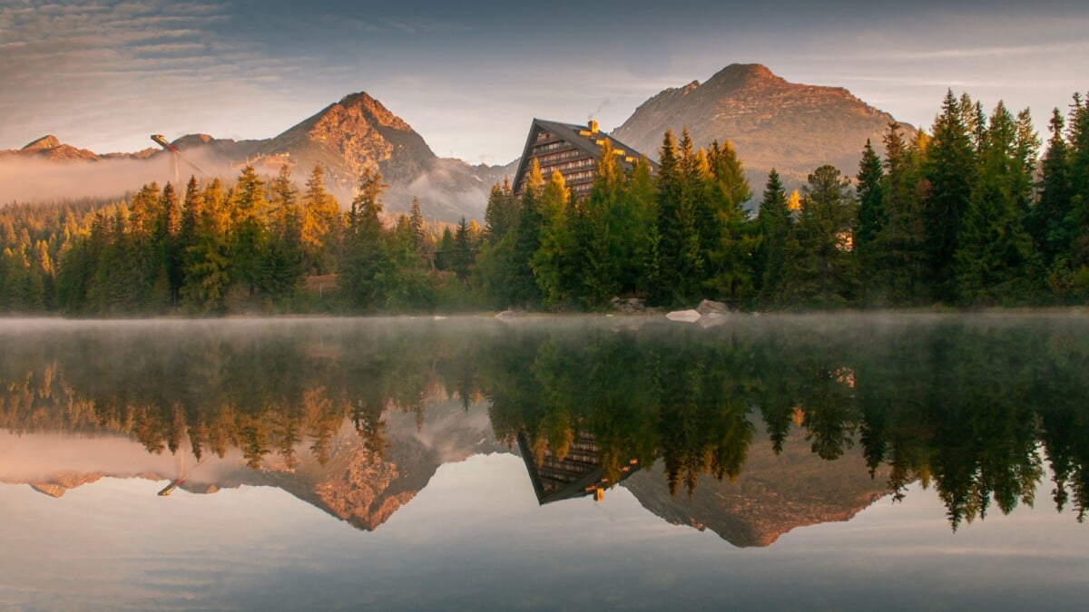 Beautiful reflection of High Tatras mountains and hotel in Štrbské Pleso lake at sunrise.