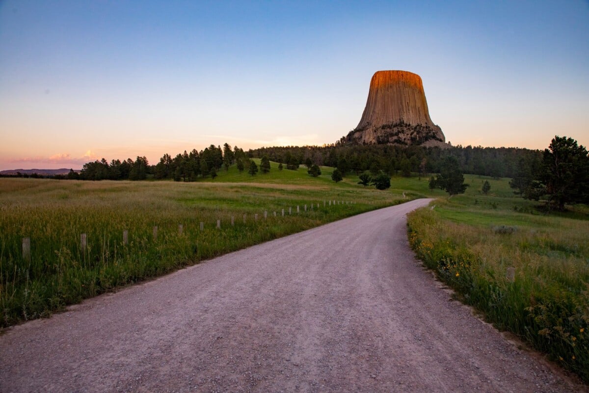 Devils Tower above grassland and a winding road at sunset