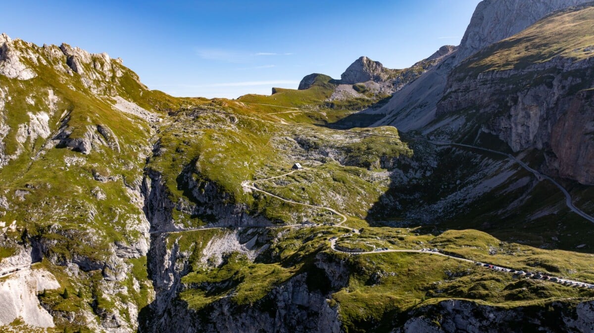 Breathtaking aerial view of a winding mountain road amidst stunning natural crags and green grass.
