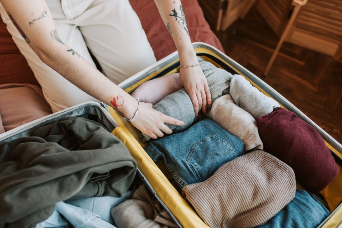 close up of a person packing various clothing items into a suitcase ready for tr | Two Scots Abroad Close-up of a person packing various clothing items into a suitcase, ready for travel.