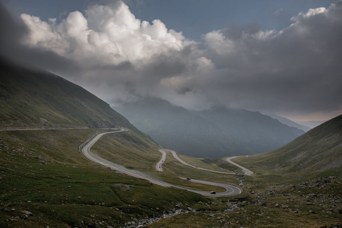 Dramatic view of a winding road in the Carpathian Mountains, Romania, under cloudy skies.