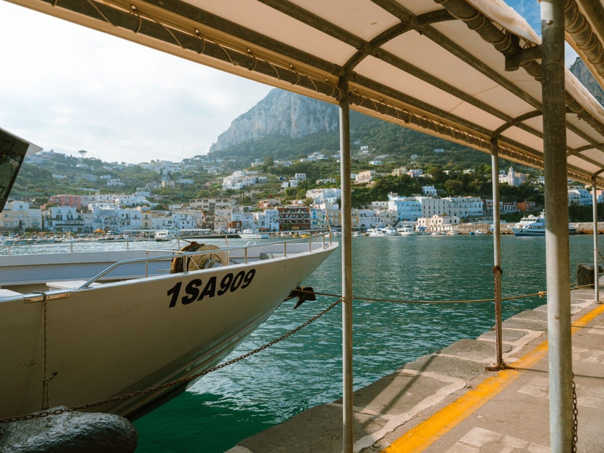 Moored yacht at Capri harbor with picturesque town and mountain backdrop.