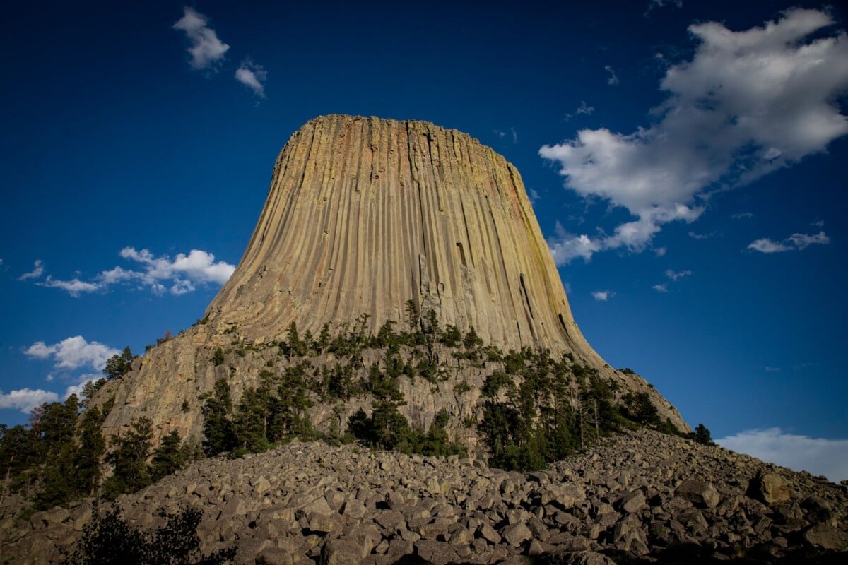 Devils Tower standing above its rocky base beneath a blue sky