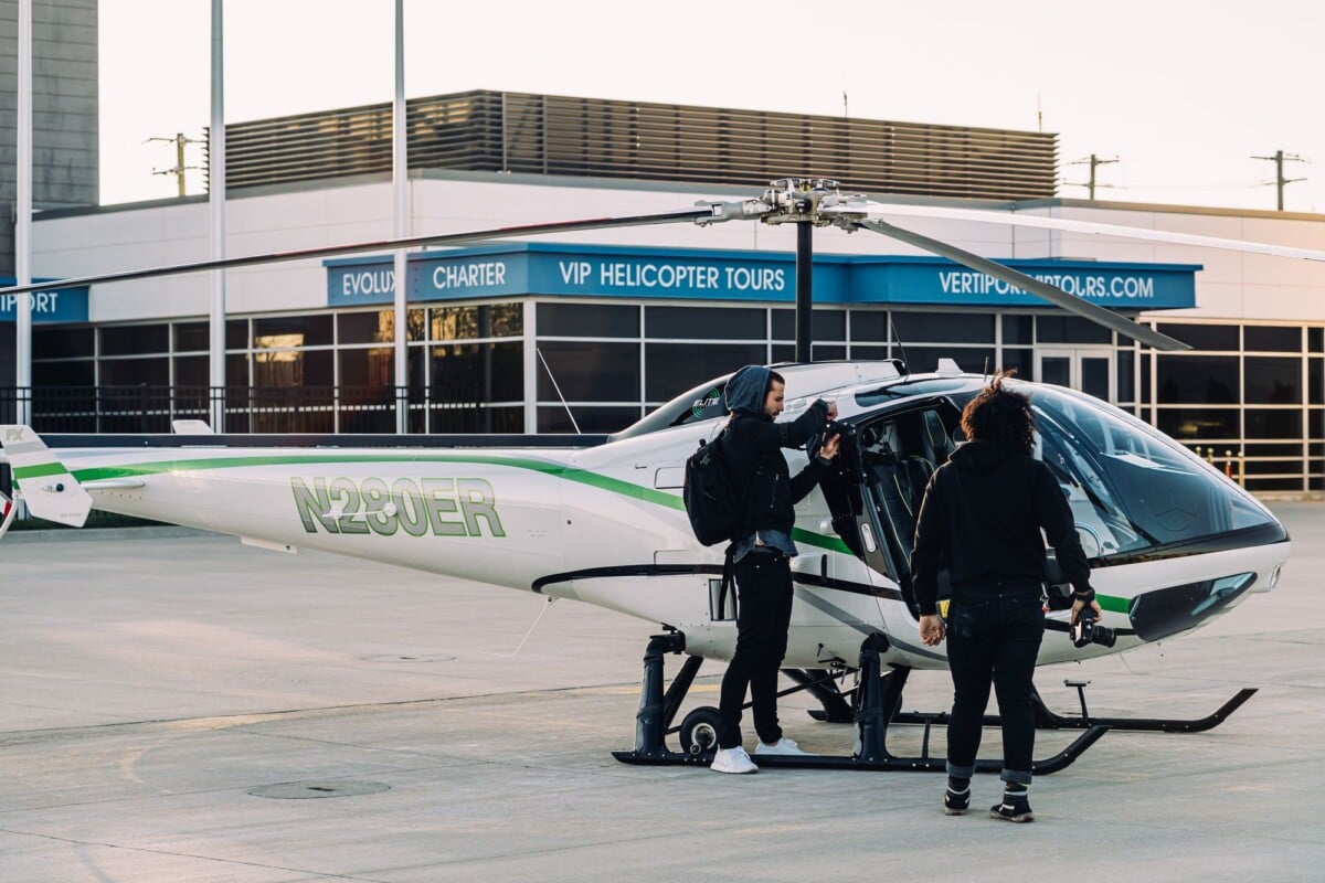 Two individuals getting into a helicopter at an airport's charter service area.